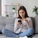 frustrated young woman sitting on a couch and reading something on her phone
