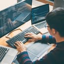 A young developer writing code on multiple computers simultaneously