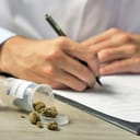 A doctor writing a prescription with an open bottle with marijuana