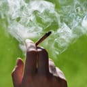 A closeup of a person holding a lit joint in their hand