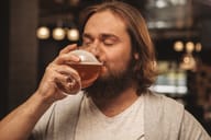 a bearded man with eyes closed sipping craft beer at a bar