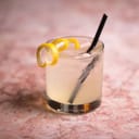 cocktail garnished with spiraled lemon peel and a straw, on a pink marble bar countertop