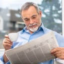 A senior man reading newspaper while drinking coffee