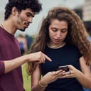 Young woman typing on her phone while her male friend is telling her the steps she should follow.