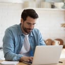 young man working remotely on a white laptop in his modern kitchen