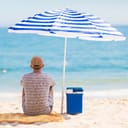 man relaxing under a parasol with a cooler of cold drinks on the beach