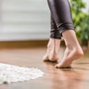 close-up of young woman walking barefoot across the warm wooden floor panels in her home