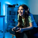Happy female gamer smiling while playing and winning in a video game with a remote controller. Young woman sitting on the couch in her bedroom with neon led lights