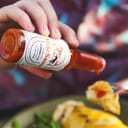 Close-up of hot sauce from a bottle being poured on a chicken dish.