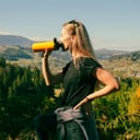 Young woman with long blonde hair drinking water from a yellow bottle
