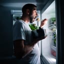 a man snacking at night in front of the refrigerator