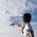 schoolboy throwing a paper plane against a blue sky