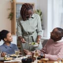 Woman getting ready to serve salad at a table where a girl and man are sitting all of whom are sharing smiles