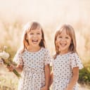 two joyful identical twin girls playing outdoors in summer, one holding a little bouquet