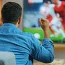 A man sitting in front of a TV watching a soccer match