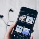 A person holds an iPhone 6 with the Spotify app open on the 'Home' page.