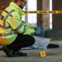 Wearing gloves. Male detective is collecting evidence in a crime scene near dead body on the construction site.