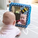Close-up of an infant gazing at a mirror while on their stomach.
