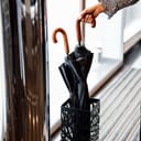 close-up of a woman's hand taking one of two black umbrellas that are in the umbrella stand