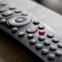 A portrait of a television infrared remote control lying on a wooden table, with the focus on the play and pause buttons.