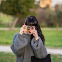 woman wearing gray knitted sweater holding yellow point-and-shoot camera
