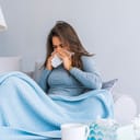 Sick Woman.Flu.Woman Caught Cold. Sneezing into Tissue. Headache. Virus .Medicines. Young Woman Infected With Cold Blowing Her Nose In Handkerchief. Sick woman with a headache sitting on a sofa