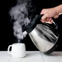 Person pouring boiling water from a kettle into a cup