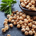 Fresh chickpeas scattered on the table next to a bowlful of more chickpeas