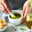 Woman hands making italian pesto in bowl. Ingredients - basil, lemon, parmesan, pine nuts, garlic, olive oil and salt on rustic wooden background. Top view, flat lay, copyspace