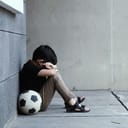 sad boy leaning against a wall next to a black and white ball, crying alone because of bullying
