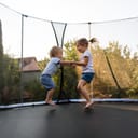baby brother and sister enjoying time together as they are jumping on the trampoline in the backyard
