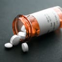 A bottle of pills lying on a surface with some pills coming out of the bottle