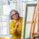 happy senior female artist painting on an easel in her well-lit studio