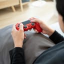 Close-up of young man's hands holding a red controller while playing video games.