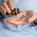 A person taking two capsules from a medicine bottle