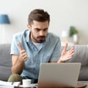 Close-up of an angered young man stressed by a computer malfunction, seated in his living room.