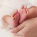 close-up of a mother's hand cradling her baby's tiny feet against a soft white background