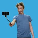 A teenage boy makes a funny grimace for a selfie, while holding his phone on a selfie stick.