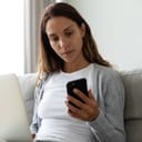 A serious young woman looking at her phone while sitting on a couch