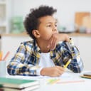 teenage African-American boy gazing thoughtfully while sitting at a desk trying to do his homework
