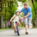 happy father teaching his young daughter to ride a bicycle during a summer family activity