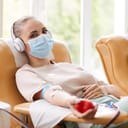A girl wearing a face mask and headphones donating blood