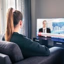 young woman sitting in her living room watching a TV news broadcast about the elections