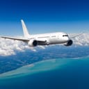 White passenger wide-body plane is flying in blue cloudy sky over the sea.