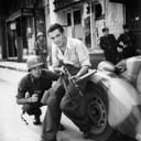 American officer and French partisan crouch behind an auto during a street fight in a French city