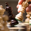 A closeup of a chess player knocking over a black queen with a white queen