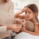 mother checking her daughter's temperature who is sick with chickenpox and lying on the bed while hugging her teddy bear