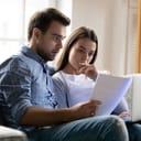 young worried couple reading and analyzing a contract, sitting on a couch in their living room