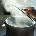 Steam rising as a man lifts the glass lid from an electric rice cooker