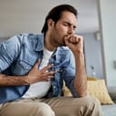 man sitting on a couch and coughing